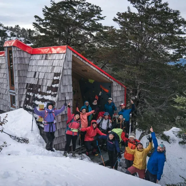 Personas posando en un refugio de techo rojo en la nieve que es parte de los proyectos sociales de DeporteLibre