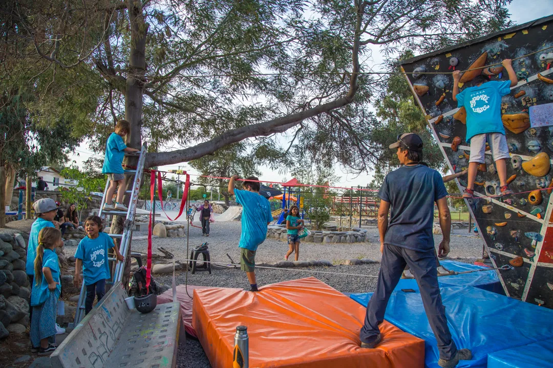 Fotografía de un adulto y niños haciendo ejercicios de escalada en una cuerda a lado de una pared de colores.