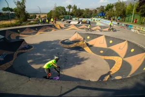 Fotografía de un niño con casco y camisa verde en bicicleta utilizando una pista de pumptracks durante el día.